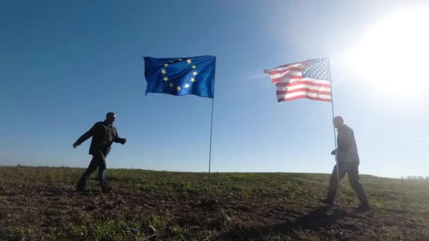 Koncepcja stosunków międzynarodowych, międzynarodowe partnerstwo USA i Unii Europejskiej. Sylwetka dwóch mężczyzn na tle flagi amerykańskiej i europejskiej. — Wideo stockowe