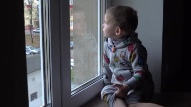 Küçük çocuk pencerenin kenarında duruyor ve evde oyuncak arabasıyla dışarı bakıyor.