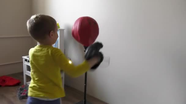 Menino de boxe no quarto com pêra de boxe de brinquedo e luvas — Vídeo de Stock