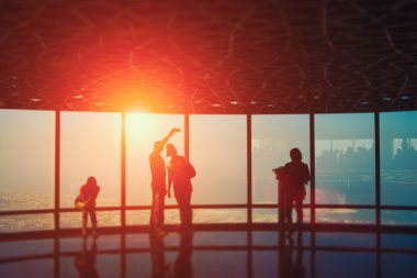 Pencere duvarı ile gökyüzü arka gün batımında, insan siluetleri