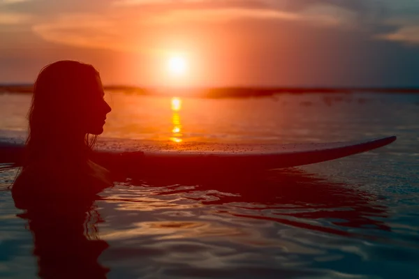 Silhouette surfer girl in water with surfboard at sunset — Stock Photo, Image