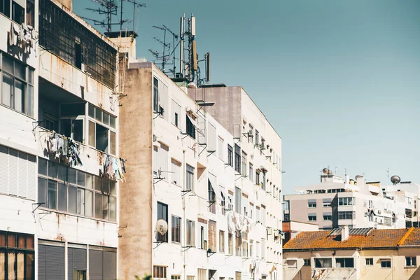 Multiple dwelling houses in a typical residential district of a europian uptown with buildings facades, balconies, dirt and rust, windows, drying laundry, roofs; a very sunny day, Lisbon, Portugal