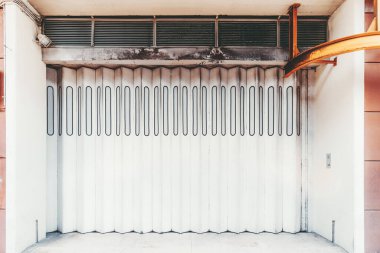 Modern bir dikey katlanabilir beyaz kapının ön cepheden görünüşü bir alışveriş merkezinin girişi veya girişinin kapıları, sağında kaldırma rampası için ağır metal bir demiryolu var.