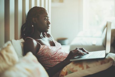 Gecelikli, örgülü saçlı, hayranlık uyandıran genç siyahi bir kadın hafta sonunu karantina sırasında yatakta boş boş yatarak ve dizileri dizilerden izleyerek geçiriyor.