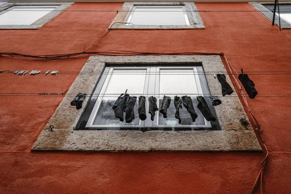 赤いカバーで覆われた古いヨーロッパの建物のファサードの一番下のビューには 服乾燥機 リスボン ポルトガルの窓の前で乾燥黒い靴下をぶら下げています — ストック写真
