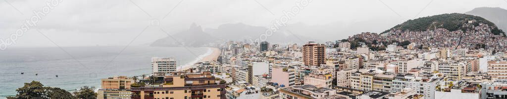 Drone panoramic view from the high above of a morning overcast hilly cityscape of the Copacabana district of Rio de Janeiro, Brazil with the dense sky, plenty of buildings, favelas, long empty beach