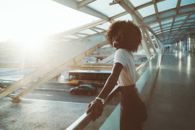 Neşeli bir kahkaha genç siyah kadın kıvırcık saçlı, solunda fotokopi yeri olan, güneşli bir akşamda otobüs durakları üzerindeki yaya köprüsünün çitlerine yaslanıyor.