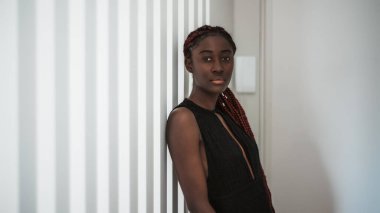 Uzun örgülü, çekici siyah bir kadının kapalı bir portresi. Dikey ahşap odunlardan oluşan çizgili bir duvarın yanında duruyor. Reklam mesajı veya logosu için fotokopi yeri var.