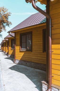 Gençlik pansiyonunda ya da pansiyonunda, metal kaplamalı, yapay fayanslar, kahverengi iniş boruları olan üçgen çatılı, sarı, tek katlı evlerin dikey görüntüsü.