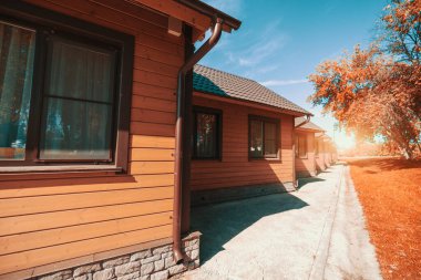 Geniş açılı çekimde bir grup benzer ahşap pansiyon ya da kamp alanı pencerelerin altında asfaltlanmış bir patika ile uzak mesafelere uzanan, güneşli bir sonbahar günü; fotokopi alanı