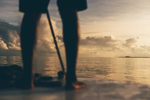 背景にある小さな島にフィールドの浅い深さと選択的なフォーカスを持つ美しい夕日の海 焦点を絞った前景にボートを操縦する男の足 モルディブ — ストック写真