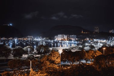 Arka planda tekne ve tekneler olan bir körfez ve Rio de Janeiro Botafogo bölgesindeki yol ve ağaçların oluşturduğu uzun süreli şehir manzarası; Brezilya şehir manzarası