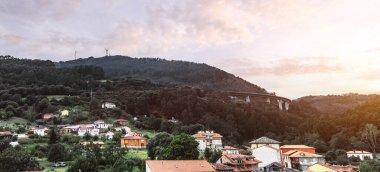 Camino de Santiago boyunca uzanan Salas köyünün panoramik manzarası yeşil tepeler, geleneksel evler, orman manzarası ve günbatımında modern köprü, huzurlu kırsal İspanya seyahat merkezi