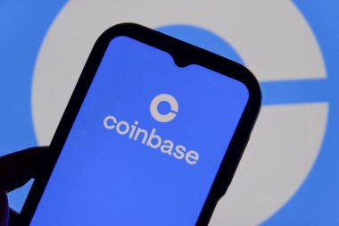 Bandung, Endonezya - 13 Şubat 2026: Bu fotoğraf ilüstrasyonlarında, Coinbase logosu bir cep telefonunda sergileniyor ve şirket markası arka planda görünüyor.