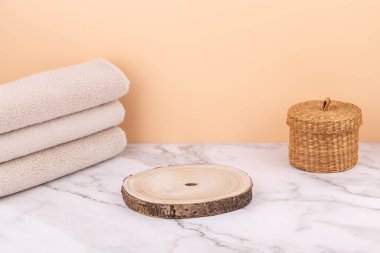 Horizontal view of rustic wooden base with beige towels and wicker basket on marble surface. Minimalistic peach background with copy space. Concept of wellness and natural lifestyle