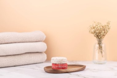Natural solid shampoo bars on a wooden tray with beige towels and a glass vase with dried flowers. Peach background and marble surface. Minimalist horizontal image with copy space. Concept of natural haircare and eco lifestyle