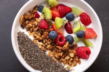 Makro kefir, taze meyve, granola ve chia tohumları koyu arka planda beyaz kasede. Doku ve rengarenk üst görünüm. Süper yiyecek ve temiz yaşam tarzı kavramı