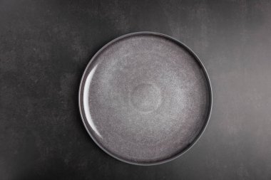 Siyah desenli arka planda koyu gri seramik plaka. Fotokopi alanı, üst görünüm ve minimalist tarzda. Markalaşma, reklam ve tasarım projeleri için tarafsız ve modern kompozisyon. Minimalist sofra takımı ve modern yaşam tarzı kavramı