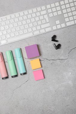 Beyaz klavye, kablosuz kulaklıklar, renkli yapışkan notlar ve açık gri dokulu arka plan üzerine pastel işaretler ile modern çalışma alanının dikey düzlüğü. Yaratıcı çalışma alanı kavramı