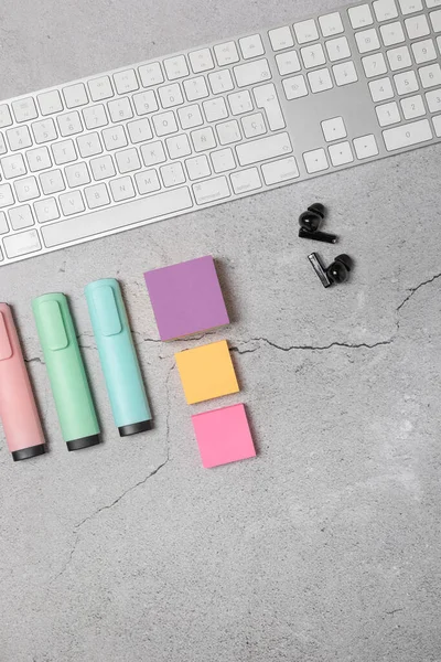 Beyaz klavye, kablosuz kulaklıklar, renkli yapışkan notlar ve açık gri dokulu arka plan üzerine pastel işaretler ile modern çalışma alanının dikey düzlüğü. Yaratıcı çalışma alanı kavramı
