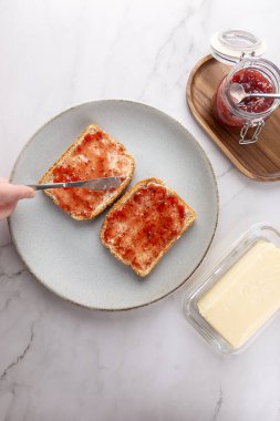 Parlak bir mutfakta çilek reçeli döken bir adamın tepeden görünüşü. Kaşık ve tereyağlı cam kavanoz da dahil. Uzayı kopyala İşlevsel mutfak ve günlük yaşam kavramı