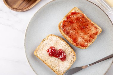 Beyaz mermer bir yüzey üzerinde tereyağı ve çilek reçeli ile iki dilim tostun yakın çekim görüntüsü. Uzayı kopyala Basit yemek ve konforlu ev kavramı