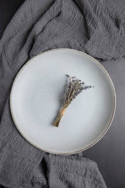 Gri seramik tabak ve gri kumaş üzerine kurulmuş kurutulmuş lavanta buketi. Kopyalama alanı olan dikey minimalist kompozisyon. Minimalist dekor ve doğal yaşam tarzı kavramı