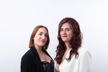 Two elegant adult women smiling with professional confident attitude, wearing white and black blazer on clean gray background. Horizontal portrait with copy space. Concept of teamwork, empowerment and business partnership