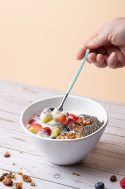 Bir kaşık kefir ve meyveyi sağlıklı malzemelerle dolu bir kasenin üzerinde tutan erkek eli. Temiz kompozisyon, nötr geçmiş ve modern yeme alışkanlıklarına odaklan. Uzayı kopyala Özenli yemek ve özen kavramı