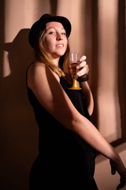 Kendine güvenen bir kadın gülümsüyor, elinde bir bardak köpüklü şarap tutuyor.