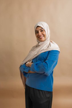 Başörtüsü takan gülümseyen kadın kollarını kavuşturarak rahatça poz veriyor.