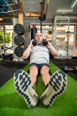 Kel adam suni çayırda mekik çekiyor, fitness merkezinde abdominal güç kazanıyor.