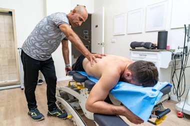 Fizyoterapist bir klinikte hastanın sırtına elle tedavi uyguluyor.