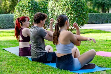 Arkadaşların parkta egzersiz yaparken yoga minderleri üzerinde kollarını esnetiyorlar.