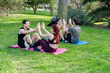 Yeşil bir parkta birlikte mekik çeken, gülümseyen ve beşlik çakan bir grup genç arkadaş.