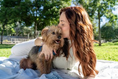 Parkta bebek poposu tutan bir kadının köpeğine şefkat göstermesini bekliyor.