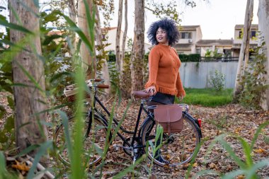 Siyah kadın bisikletinin yanında dinleniyor sonbahar doğa yürüyüşünün tadını çıkarıyor.
