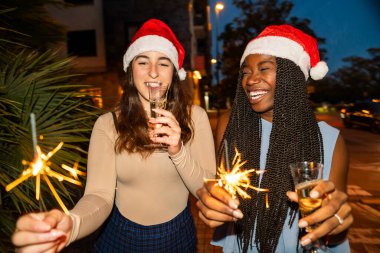 Noel Baba şapkası takan, geceleri havai fişek ve şampanyayla gülen ve kutlama yapan genç kadınlar.