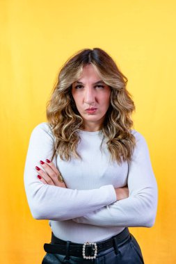 Göz açıp kapayıncaya kadar dudaklarını büzen ve sarı arka planda kollarını kavuşturan bir kadın.