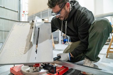 Metal profili kesen işçiler güvenlik gözlüğü ve eldivenli bir atölyede testere kullanıyorlardı.