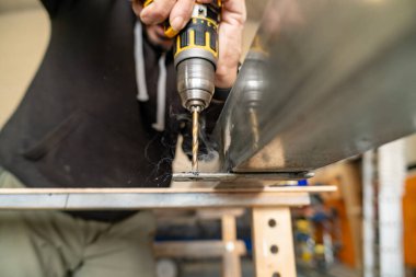 El ele tutuşan matkap, yükselen dumanla metal bir levhada delik açıyor.