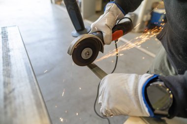 Bir atölyede metal kesmek için açı öğütücü kullanan eldiven giyen biri.
