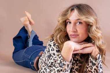 Genç bir kadın stüdyo zemininde leopar desenli kot pantolon giyerek poz veriyor.