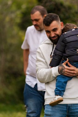 Gülümseyen iki baba, açık havada çocuklarıyla hassas bir anı paylaşıyorlar.