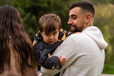 Baba oğlunu kucağında tutuyor, dışarıda bir ailenin tadını çıkarıyor.