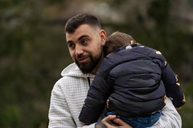 Baba çocuğunu kucağında tutuyor, bir anlık sevgi ve aile bağını yaşıyor.