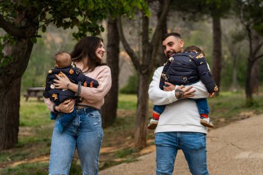 Parkta bebek taşıyan mutlu ebeveynler, birlikte sevgi dolu bir anı paylaşıyorlar.