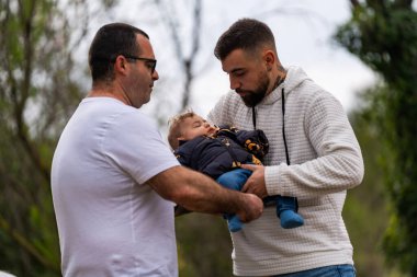 İki baba, uyuyan oğlunu dışarıda tutuyor, aile anlarını besliyor ve koruyor.