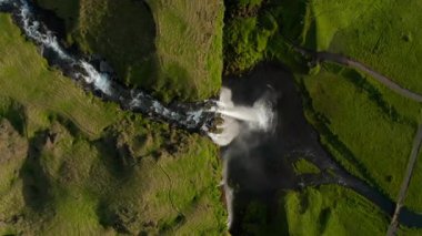 Şelale, gün ışığında yemyeşil bir vadiye akar.