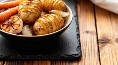 Bir kase fırında patates sarımsaklı havuç ve siyah ahşap yüzeyde soğan.